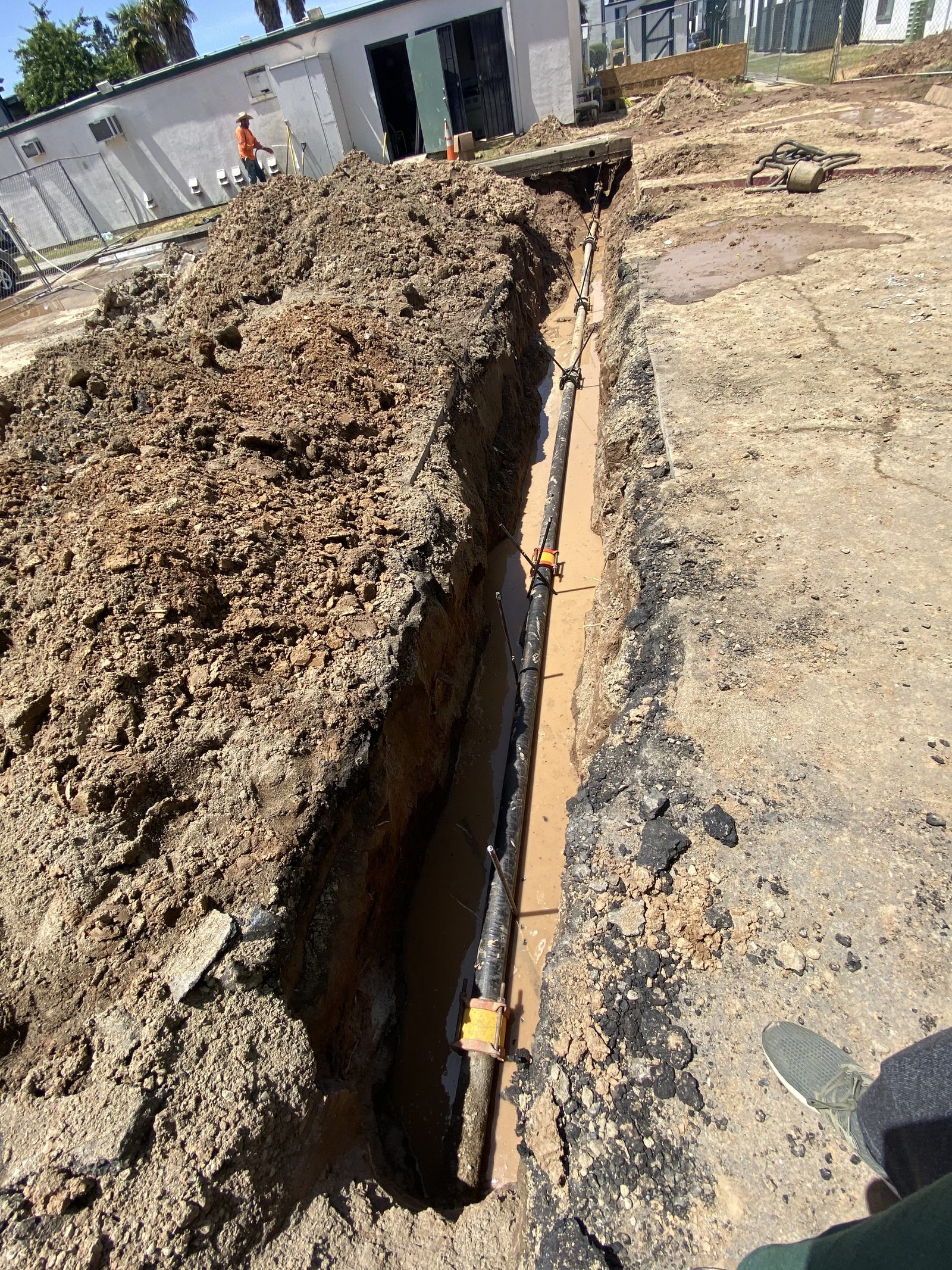 Underground Utility Trench — Long trench dug for a sewer or water service replacement — careful work next to existing structures.